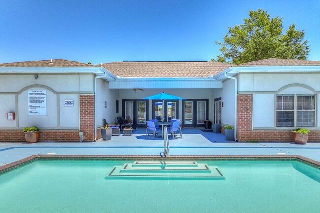 Close view of pool and clubhouse patio with umbrella seating, glass doors, and landscaped planters along deck - Parham Pointe