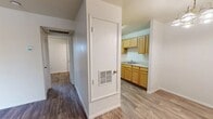 This efficiently designed 2-bedroom, 1-bathroom unit is laid out across a single floor, offering a practical and cohesive living environment. Wood-look laminate flooring runs consistently throughout the space, lending a warm, uniform aesthetic to every room.

The kitchen is a standout feature, offering generous light wood cabinetry that extends to the upper walls for ample storage, white appliances including a gas range and refrigerator, a stainless steel sink, and light countertops. A hallway connects the main living areas to the private quarters, with a wall-mounted HVAC vent providing climate control.

The dining room adds character with a painted exposed brick accent wall and a classic chandelier overhead, creating a distinct and textured atmosphere complemented by natural light from vertical-blind-dressed windows.

Both bedrooms are comfortable and well-proportioned. The primary bedroom features a ceiling fan with light fixture and a window that brings in natural light, while additional closet space is provided via a roomy open closet with a full-width hanging rod. One bedroom also includes direct access to an exterior door, adding convenience.

The bathroom is clean and functional, featuring a tub-shower combination, a wood-toned vanity with sink, a wall mirror, and wood-look tile flooring. The overall design is straightforward and move-in ready.