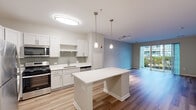 This well-appointed single-floor residence offers a thoughtfully designed open-concept layout that seamlessly connects the kitchen, dining, and living areas. The kitchen is a standout feature, equipped with stainless steel appliances including a gas range, microwave, and refrigerator, complemented by crisp white cabinetry, a grey tile backsplash, and a clean white countertop island with built-in shelving. Pendant lighting and a flush-mount ceiling fixture provide both task and ambient illumination throughout the space. The living area is bathed in natural light from floor-to-ceiling sliding glass doors that open to a private balcony, offering pleasant outdoor views. Hardwood-style flooring runs throughout the main living areas, while plush carpeting adds warmth to the bedroom, which features ample closet space with built-in shelving. The bathroom is finished with a white vanity, quartz-style countertop, undermount sink, chrome fixtures, and a large mirror with overhead lighting. A hallway with multiple doors connects the living areas to private rooms, offering a practical and efficient flow. The neutral color palette and modern finishes throughout create a clean, contemporary ambiance.