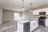 This single-floor residence showcases a thoughtfully designed open-concept layout that seamlessly connects the kitchen, dining, and living areas. The kitchen serves as the heart of the space, featuring crisp white shaker cabinetry, granite countertops, and a central island with a double basin sink and integrated dishwasher. Stainless steel appliances, including a refrigerator, range with microwave, complete the setup. Stylish pendant lights hang above the island, complementing the recessed lighting throughout. Wood-look flooring runs through the kitchen and transitions to plush carpet in the living and bedroom areas. The living space extends toward a sliding glass door that opens to a balcony, allowing natural light to fill the room. Bedrooms are generously sized with large windows and neutral tones, offering a calm, comfortable atmosphere. A walk-in closet provides ample built-in shelving and hanging space. The bathroom is well-appointed with a granite-topped vanity, white cabinetry, a large mirror with lighted fixtures, and a tub-shower combo, all set on wood-look flooring. Throughout, neutral warm-gray walls and clean finishes create a cohesive, move-in-ready environment.