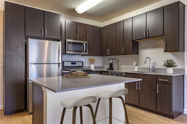 Newly renovated apartment homes feature kitchens with espresso cabinetry, grey quartz countertops, stainless steel appliances, grey tile backsplash, and hard surface flooring - Avalon Huntington Station