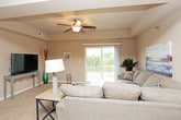 This single-floor residence offers a practical and comfortable layout with a cohesive neutral color palette throughout. The kitchen is well-equipped with rich dark-wood cabinetry, granite-style countertops, stainless steel appliances including a refrigerator, range, microwave, and dishwasher, and light hardwood-style flooring that extends into the dining area. The dining space sits near the entry and is illuminated by a pendant light fixture overhead. The open living area features plush carpeting, a ceiling fan with integrated lighting, and a sliding glass door that leads to a private balcony, allowing natural light to fill the room. A seamless view into the kitchen and dining area reinforces the open-concept feel of the common spaces. The bedroom offers generous proportions with soft carpeting, a spacious closet with wire shelving, and direct access to an en-suite bathroom. Two full bathrooms are present, each featuring dark-wood vanities with white countertops, tile flooring, and a tub-shower combination. A dedicated in-unit laundry area houses a full-sized top-loading washer and dryer with overhead wire shelving for added storage convenience.