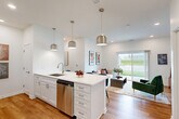 This well-designed 2-bedroom, 2-bathroom single-story home in Gretna, Nebraska offers a thoughtfully laid-out floor plan with a clean, modern aesthetic throughout. The open-concept kitchen and living area serves as the heart of the home, featuring white shaker cabinetry, quartz countertops, a subway tile backsplash, and a full suite of stainless steel appliances including a gas range, built-in microwave, refrigerator, and dishwasher. A central island with seating provides an ideal space for casual dining, while pendant lighting adds a polished finish. The kitchen flows seamlessly into the bright living room, where a large sliding glass door fills the space with natural light and offers views of the surrounding greenery. Warm hardwood-style flooring runs throughout the main living areas, complementing the crisp white walls. The primary bedroom is a comfortable retreat with plush carpet, a ceiling fan, and a natural light-filled window. The second bedroom, also carpeted, features a built-in closet and versatile layout. Both bathrooms are finished with white vanities, chrome fixtures, and hardwood-style flooring. A hallway and dedicated closet space complete the efficient and functional floor plan.