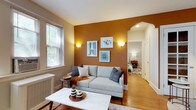 This single-floor residence offers a thoughtfully designed layout with distinct spaces that balance character and functionality. The living room serves as the focal point, featuring rich warm tones with a bold burnt-orange accent wall adorned with framed artwork and wall sconces that provide a soft, ambient glow. Large windows allow natural light to fill the room, complementing the warm hardwood flooring that runs throughout. A marble-topped coffee table and a neutral sofa anchor the space, while an elegant archway connects the living area to the rest of the unit.

The kitchen is well-appointed with rich cherry wood cabinetry, granite countertops, and a full suite of stainless steel appliances, including a gas range, built-in microwave, dishwasher, and refrigerator, offering ample storage and workspace.

Two bedrooms provide comfortable retreats, each featuring hardwood floors, neutral wall tones, and windows that overlook greenery outdoors. The primary bedroom offers generous space for a dresser and seating area, while the second bedroom functions equally well as a guest room or home office.

The bathroom retains a classic retro aesthetic, with warm yellow square tile accents, black trim detailing, white tile flooring, and a large wall mirror above a pedestal-style vanity, preserving a timeless vintage charm.