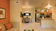 This single-floor residence showcases an open-concept layout that effortlessly connects the living, dining, and kitchen areas into one cohesive and functional space. The living area features light-toned flooring that flows throughout, contributing to a bright and airy atmosphere. A partial wall creates a subtle division between the living and dining spaces, adding architectural interest while maintaining the open feel.

The dining area is anchored by a round dark-wood table surrounded by upholstered chairs in a neutral tone, centered beneath an elegant chandelier that adds a classic touch. A framed wall mirror above a dark console further enhances the sense of depth and light in this area. A tall indoor plant nearby adds a natural, refreshing element to the space.

The kitchen, positioned adjacent to the dining area, is equipped with stainless steel appliances including a full-size refrigerator, microwave, and range. Light wood cabinetry extends to the upper wall, complemented by a granite-topped peninsula that provides additional counter space and casual seating. A pendant light above the peninsula offers focused illumination, adding both function and style.

Throughout the space, warm neutral tones, consistent flooring, and thoughtful lighting create a cohesive and inviting environment well-suited for everyday living and entertaining.