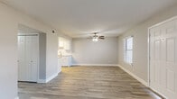 This single-floor residence offers a clean, functional layout with neutral tones and updated finishes throughout. The entry opens into a bright living area featuring wood-look tile flooring, soft gray walls, crisp white baseboards, and a ceiling fan with integrated lighting. Two flanking windows flood the space with natural light, creating an airy and welcoming atmosphere. The layout flows seamlessly into an adjacent area with warm-toned wood-look tile flooring and direct sightlines into the kitchen, which features white shaker cabinetry, a subway tile backsplash, a stainless steel sink, and black appliances including a refrigerator and electric range. A dedicated secondary room with matching hard flooring offers versatile use as a dining or flex space. Two bedrooms are finished with plush, warm-toned carpeting and ceiling fans with light fixtures, each receiving natural light through windows with blinds. The full bathroom is well-appointed with a white vanity topped with granite-style countertops, a framed mirror, wood-look tile flooring, and a tiled tub-shower combination with earthy brown tile surround. Throughout, the space maintains a cohesive, move-in-ready aesthetic defined by neutral palettes and practical, updated materials.