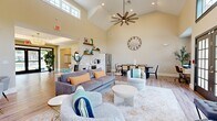 Located in Emmaus, PA, this single-floor community clubhouse offers a thoughtfully designed layout that blends comfort and functionality. The entrance greets visitors with striking herringbone-patterned hardwood-style flooring, a tray ceiling, and floor-to-ceiling glass doors that flood the space with natural light, setting a warm and welcoming tone.

The expansive living and dining area is the centerpiece of the space, showcasing soaring vaulted ceilings, multiple ceiling fans, and an abundance of natural light drawn in through large windows and French doors. A dramatic floor-to-ceiling stone accent wall frames a sleek linear fireplace and wall-mounted TV, creating a stylish focal point. The living area features comfortable seating arrangements, while the adjacent dining space includes a dining table with cane-back chairs and a stainless steel refrigerator nearby, complemented by open shelving and a small coffee station. A workstation tucked into the dining area adds a practical touch.

The exercise room is energetically appointed with vibrant green walls, rubber flooring, and large windows providing ample natural light. It is well-equipped with treadmills, a stationary bike, a cable machine, and a variety of fitness accessories, making it a fully functional workout facility.