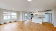 Located at 28 Hackamore in Scarborough, Maine, this single-floor residence offers a clean, modern design with an open-concept living and kitchen area that maximizes both functionality and flow. Light hardwood flooring runs throughout the main living spaces, complementing the neutral, warm-toned walls and crisp white trim.

The kitchen is a standout feature, equipped with white shaker-style cabinetry, granite countertops, a central island with additional seating and storage, stainless steel appliances — including a refrigerator, range, microwave, and dishwasher — and a stainless undermount sink. Stylish pendant lighting above the island adds a contemporary touch. A sliding glass door leads from the living area to a private balcony, while large windows invite abundant natural light and views of the surrounding community.

The bedrooms are carpeted for comfort and each features windows with blinds, baseboard heating, and generous closet space. A dedicated storage or utility area with hardwood flooring adds practical value. Additional climate control is provided by a wall-mounted mini-split unit. The overall aesthetic is bright, clean, and move-in ready, reflecting thoughtful, modern construction suited for comfortable everyday living in the Scarborough community.