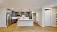 Located at 721 Halifax St in Raleigh, NC, this two-story home offers a thoughtfully designed layout with modern finishes throughout. The open-concept main level centers around a striking kitchen, where gray shaker-style cabinetry pairs elegantly with a white subway tile backsplash and gleaming quartz countertops. A large central island provides generous prep and entertaining space, while stainless steel appliances—including a range, microwave, and dishwasher—complete the contemporary setup. Pendant lighting and recessed fixtures illuminate the space warmly. Warm-toned hardwood flooring extends throughout the living areas and bedrooms, creating a cohesive and inviting atmosphere. Bedrooms are well-proportioned, featuring ceiling fans, closet storage, and neutral walls that maximize versatility. Select rooms offer large windows with exterior views, allowing natural light to fill the space. The primary bathroom showcases a dual-sink vanity with quartz counters, gray cabinetry, and backlit mirrors, alongside large-format tile flooring. A secondary bathroom features a full soaking tub and shower combination with crisp white tile surround. A dedicated in-unit laundry area houses a full-size washer and dryer. The home's clean, neutral palette and quality finishes make it a polished and functional residence in Raleigh.