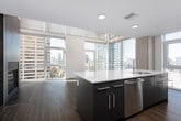This contemporary two-floor urban residence is defined by its striking floor-to-ceiling window systems that flood the interior with natural light and frame panoramic city skyline views from multiple vantage points. The open-concept main living area showcases rich hardwood-style flooring, soaring ceilings, and a dramatic floor-to-ceiling tiled fireplace surround that serves as a bold architectural focal point. The chef's kitchen is thoughtfully designed with dark navy cabinetry, a large waterfall-edge quartz island with an integrated sink, stainless steel appliances including a refrigerator, microwave, and range, and ample upper and lower cabinet storage. A sleek staircase connects the two floors, leading to the upper level where carpeted bedrooms offer peaceful retreats with expansive city views through oversized windows. Multiple bathrooms are finished with large-format tile, frameless sliding glass shower enclosures, soaking tub combinations, white quartz vanity tops, and dark cabinetry. Throughout the residence, a cohesive modern design palette of white walls, dark accents, and natural textures creates a sophisticated urban living environment with an airy, light-filled ambiance.