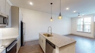 This 1-bedroom, 1-bathroom residence offers a thoughtfully designed single-floor layout that maximizes functionality and style. The open-concept living and kitchen area is anchored by a central island finished with granite countertops and a gold-toned undermount sink, illuminated by a pair of geometric pendant lights that add a contemporary flair. The kitchen is equipped with stainless steel appliances, including a refrigerator, electric range, built-in microwave, and dishwasher, complemented by gray shaker-style cabinetry with sleek hardware and a white tile backsplash. Wood-look flooring flows consistently throughout the main living areas, adding warmth and cohesion. The bedroom receives natural light through a large window with exterior views, and connects directly to a walk-in closet, offering generous storage. The bathroom features marble-look tile flooring and wall surround, a granite-topped vanity with gray cabinetry, and a framed mirror. Additional storage is provided by a double-door closet near the entry. The overall aesthetic is clean and modern, with a neutral color palette and quality finishes that create a bright, inviting atmosphere throughout.