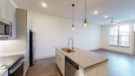 This 1-bedroom, 1-bathroom residence offers a thoughtfully designed single-floor layout that maximizes functionality and style. The open-concept living and kitchen area is anchored by a central island finished with granite countertops and a gold-toned undermount sink, illuminated by a pair of geometric pendant lights that add a contemporary flair. The kitchen is equipped with stainless steel appliances, including a refrigerator, electric range, built-in microwave, and dishwasher, complemented by gray shaker-style cabinetry with sleek hardware and a white tile backsplash. Wood-look flooring flows consistently throughout the main living areas, adding warmth and cohesion. The bedroom receives natural light through a large window with exterior views, and connects directly to a walk-in closet, offering generous storage. The bathroom features marble-look tile flooring and wall surround, a granite-topped vanity with gray cabinetry, and a framed mirror. Additional storage is provided by a double-door closet near the entry. The overall aesthetic is clean and modern, with a neutral color palette and quality finishes that create a bright, inviting atmosphere throughout.