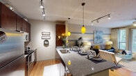 This single-story 1-bedroom, 1-bathroom unit in Houston, TX (77070) offers a thoughtfully designed layout with modern finishes throughout. The kitchen is a standout feature, showcasing rich dark-wood cabinetry, granite countertops, stainless steel appliances including a full-size refrigerator and electric range, and a peninsula with an undermount double sink. Vibrant yellow pendant lights add a striking design accent above the countertop, complementing the warm wood-style flooring that runs through the main living areas.

The open living area flows seamlessly from the kitchen, featuring track lighting, a ceiling fan, and large sliding glass doors that invite natural light and provide direct outdoor access with views of surrounding greenery. Horizontal accent stripes in yellow and gray on the walls contribute to the cohesive, contemporary aesthetic carried throughout the unit.

The bedroom is generously sized with large windows offering outdoor views, plush carpet, a ceiling fan, and the same bold accent wall design. The bathroom features large-format tile flooring, a dark-wood vanity with a marble-style countertop, a wide mirror with overhead lighting, and a tall storage cabinet. An in-unit laundry area with a stacked washer and dryer adds practical convenience to this well-appointed space.