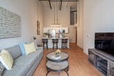 Located at 202 Jules St in St. Joseph, Missouri, this single-floor loft-style unit blends industrial character with modern finishes throughout. The open-concept living and kitchen area immediately impresses with its soaring ceilings, exposed beams, and industrial pipe details overhead. A striking arched window floods the living area with natural light while framing views of the surrounding historic brick architecture. Warm hardwood-style flooring runs consistently throughout the space, reinforcing a cohesive aesthetic.

The kitchen features white cabinetry, granite countertops, and a full suite of stainless steel appliances, including a refrigerator, range, microwave, and dishwasher. A peninsula with bar seating connects the kitchen seamlessly to the living area. An industrial-style pendant light fixture anchors the kitchen visually beneath the dramatic ceiling height.

The primary bedroom is generously proportioned with soaring ceilings, a ceiling fan, and a walk-in closet. Its en-suite bathroom offers a dual-sink vanity with white cabinetry, black hardware accents, and a glass-enclosed subway tile shower. A second bedroom provides a closet and tall ceilings. An additional bathroom features a single vanity with similar refined finishes, completing the unit's consistent, contemporary design.