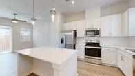 This single-floor space showcases a clean, modern design highlighted by light wood-look flooring and a neutral color palette throughout. The kitchen serves as a central feature, offering white shaker-style cabinetry extending to the ceiling, a crisp white quartz island with pendant lighting overhead, and a full suite of stainless steel appliances including a French door refrigerator with ice maker, electric range, built-in microwave, and dishwasher. A tiled backsplash and a window above the sink add both style and natural light to the space.

The living area benefits from a ceiling fan, recessed lighting, and a sliding glass door with vertical blinds that opens to a fenced outdoor area, allowing for generous natural light. Additional rooms are finished with the same light flooring and neutral walls, providing versatile, move-in-ready spaces.

The bathroom is well-appointed with a dual-sink vanity featuring white cabinetry and quartz countertops, a large mirror, and a glass-enclosed walk-in shower with tile surround. A dedicated laundry area includes a stacked GE washer and dryer unit, adding everyday convenience to this thoughtfully designed space.