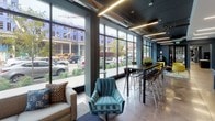 Located at 2007 Lyndale Ave S in Minneapolis, MN, this contemporary amenity floor offers a thoughtfully designed collection of communal spaces finished with a consistent modern aesthetic. Deep slate-blue walls, polished concrete floors, and linear LED lighting create a cohesive, upscale atmosphere throughout.

The welcoming entry corridor features a wall-mounted fire safety cabinet, a dark entry mat, and clearly marked exit signage, establishing a clean and functional arrival experience. Beyond the entry, the main lounge opens up dramatically, anchored by expansive floor-to-ceiling windows that flood the space with natural light and offer direct street views of Lyndale Avenue. Vibrant chartreuse lounge chairs, a tufted area rug, and curated abstract artwork add bold pops of color against the cool-toned walls. A warm wood-paneled accent wall introduces texture and contrast to the open layout.

A bar-height communal table with seating runs along the window line, complemented by a coffee station for convenient self-service. A billiards table is positioned along the wood-paneled wall, adding a recreational focal point to the lounge.

The fitness center is well-appointed with a full suite of equipment including treadmills, ellipticals, a cable resistance machine, and a dumbbell rack. Large windows bring in natural light, and bold artwork on the walls contributes to an energizing workout environment. Exposed ductwork on the dark ceiling reinforces the industrial-modern design language found throughout the space.