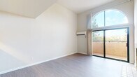 This single-floor residence showcases a thoughtfully designed layout with a variety of distinctive architectural and functional details. The living area immediately draws attention with its soaring vaulted ceilings and a striking arched window that floods the space with natural light. A tile-surround fireplace serves as a focal point, adding warmth and character, while sliding glass doors open to a private balcony with views of surrounding greenery.

The kitchen is connected to the living area via a pass-through counter, creating an open and communicative flow. It is equipped with stainless steel appliances, including an electric range, over-the-range microwave, and refrigerator, complemented by white cabinetry and light countertops.

The bedroom features a wall-mounted split AC unit for climate control and direct balcony access through additional sliding glass doors, while a secondary bedroom is carpeted and includes a baseboard heater and a window with outdoor views. The bathroom is clean and functional, offering a full tub-shower combination. Throughout the unit, light-toned hardwood-style flooring adds continuity and a modern aesthetic.