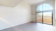 This single-floor residence showcases a thoughtfully designed layout with a variety of distinctive architectural and functional details. The living area immediately draws attention with its soaring vaulted ceilings and a striking arched window that floods the space with natural light. A tile-surround fireplace serves as a focal point, adding warmth and character, while sliding glass doors open to a private balcony with views of surrounding greenery.

The kitchen is connected to the living area via a pass-through counter, creating an open and communicative flow. It is equipped with stainless steel appliances, including an electric range, over-the-range microwave, and refrigerator, complemented by white cabinetry and light countertops.

The bedroom features a wall-mounted split AC unit for climate control and direct balcony access through additional sliding glass doors, while a secondary bedroom is carpeted and includes a baseboard heater and a window with outdoor views. The bathroom is clean and functional, offering a full tub-shower combination. Throughout the unit, light-toned hardwood-style flooring adds continuity and a modern aesthetic.