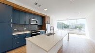 Located at 1150 Spring St NW in Atlanta's vibrant Midtown neighborhood, this modern single-floor residence showcases a thoughtfully designed open-concept layout with high-end finishes throughout. The kitchen is a standout centerpiece, featuring bold navy-blue cabinetry accented by warm wood trim, a textured gray tile backsplash, stainless steel appliances, and a large island with a crisp quartz countertop and an integrated sink with a professional-style faucet — ideal for both cooking and entertaining. Light wood flooring flows seamlessly through the main living areas, enhancing the bright, airy atmosphere created by an abundance of natural light from expansive floor-to-ceiling windows. The living area enjoys sweeping views of the Atlanta cityscape and surrounding greenery. The bedroom is carpeted for comfort and also benefits from large windows with panoramic outdoor views, complemented by a ceiling fan. The entryway includes a built-in mudroom nook for added functionality. The bathroom is finished with navy cabinetry matching the kitchen, a quartz vanity top, backlit mirror, and a glass-enclosed tiled shower, completing the cohesive modern aesthetic found throughout the space.