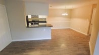 This single-floor residence offers a well-designed open-concept layout that seamlessly connects the kitchen, dining, and living areas. The kitchen is appointed with white cabinetry, dark countertops, a stainless steel sink, and a black range, all framed by a peninsula with a wraparound breakfast bar that opens to the main living space. The pass-through design enhances visibility and communication between the kitchen and the adjoining rooms. Warm hardwood-style flooring runs throughout the open living area, providing a cohesive and inviting aesthetic. The dining area is defined by an elegant multi-arm chandelier that adds a classic touch to the space. Neutral wall tones in soft beige and grey create a calm, versatile backdrop throughout. Clean white baseboards and recessed ceiling features contribute to the overall tidy and well-maintained character of the interior. The layout is practical and efficient, making excellent use of the available floor space while maintaining an airy, open feel. The combination of functional kitchen design, durable flooring, and thoughtful lighting makes this a comfortable and move-in ready space.