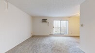 This single-floor, 2-bedroom, 1-bathroom unit features a practical and efficient layout designed to maximize usable living space. The living room serves as the central gathering area, finished with neutral-toned carpet and bright white walls that create a clean, open atmosphere. A large sliding glass door floods the room with natural light and provides outdoor views, while a wall-mounted air conditioning unit and baseboard heating ensure year-round climate control.

The kitchen is outfitted with warm wood cabinetry, granite-patterned countertops, a stainless steel sink, and white appliances including a range and dishwasher. Durable wood-look flooring grounds the space and provides a practical, easy-to-maintain surface.

Both bedrooms are carpeted and feature windows with blinds that allow for natural light. The primary bedroom includes access to a dedicated walk-in closet with built-in shelving rods for organized storage. A wall-mounted heating unit is also present in one bedroom for individual climate control.

The full bathroom is finished with white subway tile surrounding the tub-shower combination, a hexagonal tile floor, a wood-toned vanity with a white countertop, and a mirrored medicine cabinet. Two hallways connect the rooms, contributing to a clear and straightforward flow throughout the unit.