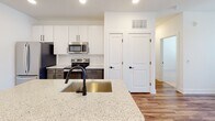 Located at 336 Chestnut Parkway in Indian Trail, NC, this thoughtfully designed single-floor home showcases modern finishes and a clean, contemporary aesthetic throughout. The open-concept layout seamlessly connects the living and kitchen areas, anchored by warm wood-look luxury vinyl plank flooring that runs throughout the main living spaces.

The kitchen is a standout feature, equipped with stainless steel appliances including a French door refrigerator, electric range, and over-the-range microwave. A two-tone cabinetry scheme pairs crisp white upper cabinets with gray lower cabinets, all complemented by a classic white subway tile backsplash. The kitchen island serves as a functional centerpiece, topped with light granite countertops and fitted with a matte black undermount sink and pull-down faucet.

The bathroom continues the modern design language, featuring white subway tile surrounding the tub and shower, matte black fixtures and hardware, a granite-topped vanity, and wood-look flooring for a cohesive look. The bedroom offers plush carpet flooring and a window with blinds that allows natural light to fill the space. Throughout the home, recessed lighting, clean white walls, and thoughtful hardware selections create a bright, move-in-ready environment.