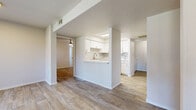 This single-floor residence offers a bright, open-concept layout designed for comfortable everyday living. Wood-look flooring flows seamlessly throughout the entire space, creating a cohesive and easy-to-maintain aesthetic. The living area is generously proportioned, featuring a ceiling fan with light, a sliding glass door that invites natural light, and a window with vertical blinds providing outdoor views. A pass-through opening connects the living area to the kitchen, enhancing the sense of openness. The kitchen is well-appointed with white cabinetry, light countertops, a tile backsplash, a stainless steel sink, and a full suite of white appliances including a range, microwave, and dishwasher. The bedrooms are comfortably sized, each equipped with ceiling fans and easy access to closet space, including one room with a walk-in closet. A dedicated hallway leads to the bathroom, which features a single vanity with a mirror, light countertop, and brushed nickel fixtures. A separate laundry area houses a full-sized washer and dryer with overhead wire shelving. Throughout the space, a neutral white and grey color palette, textured ceilings, and consistent flooring contribute to a clean, move-in-ready ambiance.