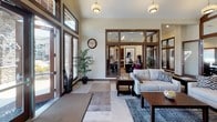 Located in Edgewood, Washington, this single-story community facility offers a comprehensive range of amenities designed to serve its users effectively. The building's interior is defined by warm, dark-trimmed wood accents set against neutral cream-toned walls, creating a cohesive and welcoming aesthetic throughout.

The welcoming lobby and lounge area features soaring vaulted ceilings, large multi-pane windows that invite abundant natural light, and comfortable seating arranged around a central coffee table. Adjacent to the lounge, a well-appointed kitchen includes rich dark wood cabinetry, stainless steel appliances, a generous countertop island, and direct access to additional amenity spaces.

A formal conference room accommodates a large group around a substantial dark wood table, equipped with a wall-mounted display screen and interior glass partition windows. The dedicated fitness center showcases vaulted ceilings, a row of windows providing natural light, and a full array of cardio and strength equipment. A standout indoor basketball court features soaring ceilings, polished hardwood flooring with regulation markings, and clerestory windows. Wide, carpeted corridors connect all spaces, accented with framed artwork, water stations, and restroom facilities, ensuring a functional and polished experience throughout.