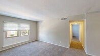 Located at 613 Michigan Dr in Hampton, Virginia, this single-floor residence offers a straightforward, functional layout with a clean and neutral aesthetic throughout. The interior is finished with soft, wall-to-wall carpeting across the living and bedroom areas, complemented by light gray and beige tones on the walls that create a calm, cohesive atmosphere.

The kitchen is a standout feature, equipped with white cabinetry, dark granite-style countertops, and white appliances including a refrigerator and gas range. A peninsula counter extends into the adjacent living area, providing a convenient pass-through and additional prep or dining space. The kitchen floor features light wood-look vinyl, adding a practical, easy-to-maintain surface.

Multiple carpeted rooms are accessible via a central hallway, each benefiting from windows fitted with horizontal blinds that allow for adjustable natural light and views of the surrounding neighborhood greenery. The rooms are generously proportioned, offering versatile space suitable for a variety of uses. Ceiling-mounted HVAC vents ensure consistent climate control throughout. The overall layout, as seen in the 3D model, reflects a well-organized floor plan with distinct zones for living, cooking, and private spaces, making this a practical and comfortable residence.