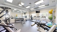 This 580-square-foot fitness center offers a comprehensive array of exercise equipment in a single-floor layout. The space features a bright, open design with recessed lighting and large windows that flood the area with natural light. The gym is equipped with multiple cardio machines, including treadmills and ellipticals, arranged in rows facing the windows. A separate area houses strength training equipment, including weight machines and free weights. The center also includes a section for functional training with stability balls, resistance bands, and floor mats. The facility's design emphasizes cleanliness and organization, with a neutral color scheme and durable flooring. Ceiling fans and air conditioning units ensure proper ventilation and comfort during workouts. This well-planned fitness center provides a variety of exercise options to accommodate different workout preferences and fitness levels.