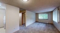 Located at 111 College Hill St in Cheney, WA, this two-bedroom, one-bathroom unit offers a practical and well-organized single-floor layout. The living area features plush carpeting, a textured ceiling, and a large window fitted with vertical blinds that allows natural light to filter in, along with a baseboard heating system. The spacious primary bedroom continues the carpeted flooring and includes its own window with views of surrounding greenery, a wall-mounted air conditioning unit, and baseboard heat, providing year-round comfort. The second bedroom is a cozy, carpeted room with clean neutral walls and a wood-trimmed door. The galley-style kitchen is efficiently designed with warm wood cabinetry, ample upper and lower storage, light countertops, a double-basin sink, and white appliances including a range and full-size refrigerator, all set over easy-care tile flooring. The bathroom features a full tub-shower combination with white tile surround, a toilet, and a single-sink vanity with cabinet storage beneath, finished with tile flooring. Throughout the unit, wood-trimmed doorways and warm neutral tones create a cohesive and functional living environment.