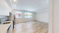 Located on the iconic Wilshire Boulevard in Los Angeles, this single-floor unit offers a thoughtfully designed layout that maximizes its compact footprint. Light wood-style plank flooring runs seamlessly throughout, lending warmth and continuity to the space.

The open-concept kitchen and living area forms the heart of the unit. The kitchen is outfitted with sleek, flat-front white cabinetry extending to the ceiling for ample storage, a textured tile backsplash, white quartz countertops, and a full suite of stainless steel appliances including a range, over-the-range microwave, dishwasher, and refrigerator. The living area benefits from natural light streaming through a wide window with views of lush greenery outside, creating a bright and airy atmosphere.

The bathroom features a clean, minimalist aesthetic with floor-to-ceiling white subway tile surrounding a soaking tub and shower combination, complemented by chrome fixtures and light tile flooring. A hallway connects the principal spaces, providing a clear and functional flow throughout the unit.

The overall design palette — crisp white walls, contemporary finishes, and consistent flooring — delivers a cohesive, modern ambiance well-suited to urban living in the heart of Los Angeles.