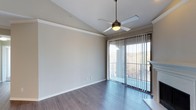 This single-floor space is designed with a clean, contemporary aesthetic that emphasizes openness and functionality. The main living area features smooth hardwood-style flooring in a cool gray-toned finish, lending a modern, cohesive look throughout. Vaulted ceilings add a sense of height and airiness to the room, enhancing the overall feeling of spaciousness.

A ceiling fan with a built-in light fixture is centrally mounted, providing both practical ventilation and ambient lighting. The walls are finished in a neutral light gray tone, offering a versatile backdrop suited to a variety of furnishing styles.

A standout feature of the space is the floor-to-ceiling sliding glass door, dressed with vertical blinds and leading to a private balcony. The balcony provides elevated outdoor views of surrounding greenery and the broader landscape beyond, allowing natural light to filter generously into the interior. White trim detailing along the walls and baseboards adds a crisp, finished appearance. Overall, the space conveys a bright, airy ambiance with thoughtful design details suited for comfortable everyday living.