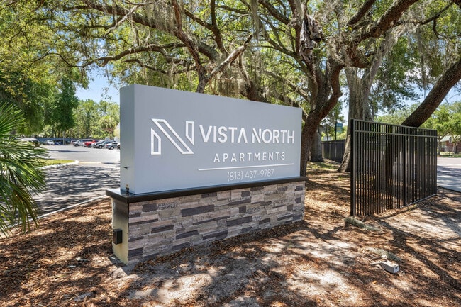 Welcome to Vista North Apartments, featuring elegant signage surrounded by lush greenery and inviting natural landscapes. - Vista North