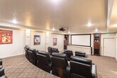 Located at 488 W Center St in Pleasant Grove, Utah, this purpose-built home theater room delivers a true cinematic experience within a thoughtfully designed, self-contained space. The room is arranged with multiple rows of plush black leather recliner seats, tiered on raised platforms to ensure unobstructed sightlines from every position. Each recliner features integrated cup holders, prioritizing comfort during extended viewing sessions.

A ceiling-mounted projector anchors the technical setup, projecting onto a large, dedicated projection screen positioned at the front of the room and flanked by a built-in wooden media console with open shelving. The screen wall is framed with clean white wainscoting details, adding a polished, finished look. Wall-mounted sconce lighting provides warm, ambient illumination throughout the space, complementing the recessed ceiling lights.

The room is finished with patterned wall-to-wall carpeting that adds both comfort and sound-dampening qualities underfoot. Crown molding runs along the ceiling perimeter, lending an elegant touch. A wall-mounted mini-split HVAC unit ensures year-round climate control. Classic movie posters adorn the walls, reinforcing the cinematic atmosphere. A stepped entry area with additional movie poster displays completes the immersive, theater-inspired aesthetic of this well-appointed screening room.