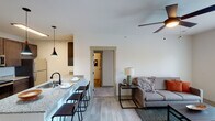 This single-floor unit presents a well-designed open-concept layout that seamlessly connects the kitchen, dining, and living areas. The kitchen is outfitted with dark espresso cabinetry, granite countertops, a light blue subway tile backsplash, and a full suite of stainless steel appliances including a range, over-the-range microwave, and refrigerator. A peninsula with bar seating and a pendant light overhead provides an ideal casual dining space.

The living area is bright and comfortable, featuring light wood-look flooring, a ceiling fan, and French doors that open to a private balcony with outdoor views. The space flows naturally into a hallway leading to the bedrooms and bathroom.

Both bedrooms are carpeted and include ceiling fans and windows that allow natural light and outdoor views. The rooms offer a calm, functional atmosphere well-suited for rest.

The bathroom is finished consistently with the rest of the unit, featuring wood-look tile flooring, a granite-topped dark wood vanity with a large mirror, and a full tub-shower combination with grab bars and a handheld showerhead. The overall palette is neutral and contemporary throughout.