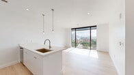 Located at 616 W Fulton Street in Grand Rapids, Michigan, this modern one-bedroom, two-bathroom unit offers a sleek, contemporary design throughout. Light oak hardwood flooring flows seamlessly across the entire space, complementing the crisp white walls and clean architectural lines.

The open-concept kitchen and living area serves as the heart of the unit, anchored by a large white waterfall island with an integrated sink and pendant lighting overhead. The kitchen is equipped with stainless steel appliances, white cabinetry, and a subway tile backsplash. Floor-to-ceiling windows in the living area flood the space with natural light and frame sweeping views of the Grand Rapids skyline and surrounding neighborhood.

The bedroom continues the minimalist aesthetic, featuring its own floor-to-ceiling window that captures city and treetop views, allowing abundant natural light throughout the day. Dark-paneled interior doors provide a striking contrast against the white walls, adding a bold design detail.

Two bathrooms serve the unit — one featuring a full soaking tub with shower combination and clean chrome fixtures, and the other showcasing a floating white vanity with an integrated sink and a modern rectangular mirror. Both bathrooms maintain the unit's consistent, minimalist design language.