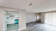 This single-floor unit offers a clean, updated interior designed for comfortable everyday living. The living area is generously sized, featuring gray-toned wood-look plank flooring, neutral taupe walls, and a textured ceiling throughout. A sliding glass door fitted with vertical blinds allows natural light to fill the space and provides direct access to an outdoor area. An additional window in a secondary room further enhances the natural light throughout.

The kitchen is thoughtfully outfitted with crisp white shaker-style cabinetry extending to the ceiling for ample storage, white countertops, a stainless steel electric range with an overhead ventilation hood, and a stainless steel dishwasher. The space is practical and visually cohesive with its bright, clean palette.

The bedrooms continue the gray plank flooring and neutral color scheme, each featuring windows with blinds and clean white trim. One bedroom connects directly to a bathroom, offering added convenience. The bathroom includes a white vanity with a brushed nickel faucet, a wall mirror with overhead lighting, a chrome towel ring, and a walk-in shower stall with a curtain rod. The overall aesthetic is neutral, modern, and move-in ready.