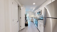 This single-floor unit presents a cohesive modern design throughout, highlighted by light wood-look flooring, neutral walls, and recessed lighting that create a bright and airy atmosphere. The galley-style kitchen is efficiently arranged and outfitted with stainless steel appliances — including a range, microwave, dishwasher, and refrigerator — complemented by granite countertops and ample upper and lower cabinetry in a clean white or light wood finish. The open-concept living area flows naturally from the kitchen, offering a comfortable and functional space bathed in natural light from a large window with outdoor views. The bedroom is a calm retreat, featuring the same light flooring, generous natural light from a wide window, and direct access to the bathroom. The bathroom is well-finished with a granite-topped vanity, a large mirror, and a walk-in shower, maintaining the clean, minimal aesthetic found throughout the unit. A separate shower stall with white tile surround adds a polished touch. Throughout the space, consistent use of light tones, modern hardware, and streamlined fixtures creates a unified, contemporary living environment that is both functional and visually cohesive.