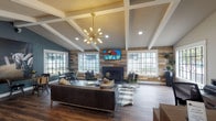 Located in Houston, TX, this single-floor community space combines modern design with warm, inviting elements to create a versatile gathering area. The main lounge is anchored by a striking reclaimed wood accent wall that frames a sleek, tile-surround fireplace topped with a large flat-screen TV — a natural focal point for the room. Vaulted ceilings with exposed white beam detailing add architectural interest and a sense of openness, while a statement Sputnik chandelier provides a contemporary finishing touch overhead.

Rich hardwood flooring runs throughout the space, complementing a thoughtfully curated mix of leather sofas, upholstered seating, and patterned area rugs. Multiple seating arrangements encourage both relaxed lounging and casual conversation. A dedicated dining nook, set against deep teal walls, features grid-pane windows that offer views of the surrounding community grounds, filling the area with natural light.

A built-in kitchenette serves as a practical amenity, outfitted with dark cabinetry, a wine cooler, microwave, and a bold geometric tile backsplash. Recessed lighting and large multi-pane windows on multiple walls ensure the entire space remains bright and welcoming throughout the day, making it a well-equipped and aesthetically refined communal retreat.