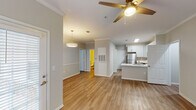 This ground-floor unit in Mobile, Alabama, offers a thoughtfully designed open-concept layout finished with warm wood-style flooring and neutral gray tones throughout. Crown molding accents the main living areas, adding a polished architectural detail, while ceiling fans in both the living room and bedroom provide comfort year-round.

The kitchen is well-appointed with white shaker-style cabinetry, light countertops, and a tile backsplash. Stainless steel appliances include a refrigerator, electric range, over-the-range microwave, and dishwasher. A peninsula with a sink extends into the space, creating a natural division between the kitchen and the open living and dining areas. A pendant light fixture anchors the dining zone, while additional natural light filters in through multiple windows fitted with blinds.

The bedroom is generously sized with two windows that invite natural light and a ceiling fan overhead. A walk-in closet provides ample storage space, complemented by an additional door for further access. The bathroom features a tub-shower combination with tile surround, a vanity with white countertop, framed mirror, and wood-style flooring consistent with the rest of the unit.
