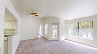 This single-floor residence offers a thoughtfully designed layout that balances open living with functional private spaces. The spacious living room is a highlight, featuring soaring vaulted ceilings, plush carpeting, and a ceiling fan with light fixture. Large windows and a glass-paneled exterior door flood the room with natural light and provide views of surrounding greenery. A pass-through bar connects the living area to the kitchen, which is equipped with white cabinetry, speckled granite-style countertops, a double-basin sink, and a white range, creating a clean and efficient workspace.

The entryway transitions from wood-look flooring into the carpeted main living areas, providing a practical and welcoming threshold. The bedrooms are generously sized, each featuring plush carpeting, vaulted ceilings, and access to natural light. One bedroom includes a mirrored sliding-door closet with built-in shelving, offering excellent storage capacity.

Two full bathrooms serve the residence, each featuring white tile tub/shower combinations with chrome fixtures, wood-look flooring, and speckled countertop vanities. The overall palette throughout the home is light and neutral, with white walls and trim that enhance the airy, open ambiance of the space.