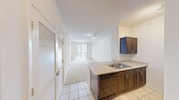 This 500 square foot apartment, located at 11400 Domain Drive in Austin, Texas, offers a compact yet well-designed living space. The single-floor layout maximizes efficiency, combining kitchen and living areas into an open-concept design. The modern kitchen features wood cabinetry, stainless steel appliances, and a breakfast bar, ideal for casual dining or additional workspace.

The living area is bright and airy, with large vertical blinds covering sliding glass doors that lead to a private balcony, allowing ample natural light and outdoor views. Plush carpeting in the living space adds warmth and comfort.

The bathroom is thoughtfully designed with a full-sized bathtub/shower combination, decorated with a checkerboard tile accent. A single vanity with storage and modern fixtures complete the space. The apartment also includes a closet for storage.

Track lighting in the kitchen and recessed lighting throughout provide adjustable illumination options. The neutral color palette and clean lines create a contemporary feel, making this apartment an ideal urban dwelling for singles or couples seeking a modern, low-maintenance lifestyle in the heart of Austin.