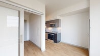 Located at 1110 W Columbia Way in Vancouver, WA, this thoughtfully designed one-bedroom, one-bathroom unit maximizes every inch of its compact footprint with a clean, modern aesthetic. Light wood-tone flooring runs throughout, complementing crisp white walls and a bright, open atmosphere.

The galley-style kitchen is well-appointed with stainless steel appliances — including a range, microwave, and refrigerator — paired with dark cabinetry, stone-look countertops, and a subway tile backsplash that adds a contemporary touch.

The living area flows naturally from the kitchen, anchored by a large picture window that fills the space with natural light and frames views of the Vancouver waterfront and surrounding cityscape. A sliding door leads to the cozy bedroom, which features a built-in closet with wire shelving, offering practical storage within a compact layout.

The bathroom is finished with a dark-toned vanity, stone countertop, rectangular undermount sink, matte black fixtures, a large framed mirror, and a tub-shower combination with floor-to-ceiling dark tile surround. A hallway connects all areas efficiently, with a full-size stainless steel refrigerator visible at the entry, reinforcing the unit's functional design. The overall ambiance is modern, clean, and urban.