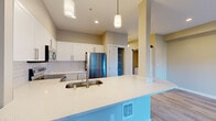 Located at 8702 164th Ave NE in Redmond, Washington, this single-floor residence offers a thoughtfully designed layout with contemporary finishes throughout. The open-concept kitchen serves as a central highlight, featuring crisp white shaker cabinetry, a classic subway tile backsplash, and a generous island with a white quartz countertop and undermount sink. Stainless steel appliances, including a refrigerator, range, and over-the-range microwave, complete the well-equipped cooking space. Pendant lighting above the island and recessed ceiling fixtures provide both functional and ambient illumination.

The living area is bright and welcoming, anchored by a tiled corner fireplace and sliding glass doors that lead to a private balcony offering views of surrounding greenery and the neighborhood. Light-toned hardwood-style flooring extends throughout the main living spaces, contributing to a cohesive and modern aesthetic.

The bedroom wing is accessed through double doors, leading to well-proportioned rooms with neutral warm-toned walls and continued hardwood-style flooring. The bathroom features brushed nickel hardware and fixtures. A walk-in closet with built-in shelving provides practical storage. The overall design balances clean, modern elements with a comfortable and functional living environment.