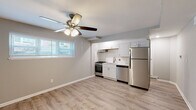 This single-floor unit presents a clean, updated interior with a thoughtfully organized open-concept layout. Light gray walls and light-toned wood-style flooring flow consistently throughout, creating a cohesive and airy atmosphere. Ceiling fans with integrated lighting fixtures are installed in both the main living area and the bedroom, contributing to both comfort and practicality.

The kitchen is efficiently designed along a single wall, featuring white shaker-style cabinetry above and below the counter, complemented by white quartz countertops and a classic white subway tile backsplash. Stainless steel appliances include a gas range, dishwasher, and full-size refrigerator, all framed by an under-cabinet range hood. A stainless steel undermount sink with a brushed nickel faucet anchors the workspace. A window positioned above the living area allows natural light to enter the space.

The bedroom is a well-proportioned room with the same wood-style flooring, soft gray walls, a ceiling fan, and a window with blinds that brings in natural light.

The bathroom is finished with large-format marble-look tile surrounding a soaking tub and shower combination, accented by a round wall mirror and a white vanity with a clean countertop, delivering a polished, contemporary feel.