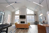 This contemporary single-floor community space is thoughtfully designed to foster connection and comfort. Soaring ceilings and floor-to-ceiling windows throughout the space flood the interior with natural light, offering open views of the surrounding neighborhood. Light-toned wood-style flooring runs seamlessly throughout, lending warmth and continuity to the overall aesthetic.

The main lounge area serves as the heart of the space, anchored by a sleek, linear fireplace set into a clean white surround, complete with a floating wood mantel and wall-mounted television above. Comfortable seating arrangements, including plush sofas and accent chairs in bold yellow tones, are positioned around a patterned area rug, creating an inviting atmosphere for gathering and relaxation. A pool table adds a recreational element, rounding out the entertainment offerings.

The kitchenette is well-appointed with white cabinetry, butcher block countertops, subway tile backsplash, a sink, and pendant lighting overhead. A bold crimson accent wall adds a vibrant focal point, while bar-height seating along the island encourages casual socializing.

Near the entrance, a bright and airy reception area features framed wall art and minimalist seating. Additional high-top tables and metal stools are positioned near large windows, providing casual spots for conversation or individual use. The space strikes a balance between modern design and functional communal living.