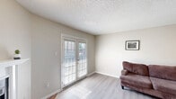 Located at 500 Rolling Hills Pl in Lancaster, TX, this single-floor home offers a thoughtfully arranged layout comprising a combined kitchen and living room, one bedroom, a hallway, and a closet. The living room is open and airy, featuring light wood-style flooring, neutral beige walls, a textured ceiling, and a ceiling fan that promotes comfortable airflow. A corner fireplace with a classic white mantel and brick hearth serves as a charming focal point, while windows allow natural light to fill the space. The kitchen follows a galley-style layout with white cabinetry, light stone-look countertops, black appliances including a refrigerator, range, and dishwasher, and matching wood-style flooring that ties seamlessly to the living area. A pass-through opening connects the kitchen to the living room, enhancing the open feel. The bedroom is a comfortable, well-defined retreat featuring wood-style flooring, a ceiling fan with light fixture, a window with blinds for natural light and privacy, and a louvered closet door providing convenient storage access. The overall ambiance throughout the home is clean, functional, and inviting, with a consistent neutral color palette and practical finishes suited for everyday living.