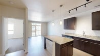 This single-floor residence features a thoughtfully designed open-concept layout that seamlessly connects the kitchen and living area. The kitchen serves as the centerpiece of the space, showcasing rich dark-espresso cabinetry that extends to the upper walls, paired with light speckled granite countertops that provide a striking contrast. A central island with matching granite offers additional prep space and casual seating. Stainless steel appliances, including a refrigerator, electric range, and microwave, are integrated into the layout, while pendant lighting and a track lighting system illuminate the workspace effectively. Light wood-style flooring flows throughout the main living area, enhancing the bright, airy atmosphere.

The living area opens directly to a private balcony through sliding glass doors, allowing natural light to fill the space and providing outdoor views of the surrounding urban environment. Bedrooms feature soft carpeting, generous closet space with sliding panel doors, and large windows that frame city views. The bathroom includes a full soaking tub with a shower and tile flooring. Neutral wall tones throughout the unit create a clean, modern aesthetic well-suited to a variety of interior styles.