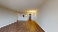 This single-floor unit is designed with a practical, open layout that maximizes usable living space. The main living area is generously proportioned, featuring warm hardwood-style laminate flooring that runs throughout the unit, neutral grey walls, and white baseboards that create a clean, contemporary aesthetic. A pendant light fixture serves as a focal point near the entry, while a large window floods the space with natural light and frames views of the surrounding cityscape.

The galley-style kitchen is efficiently arranged, featuring white cabinetry with modern hardware, light stone countertops, a tile backsplash, and a full suite of stainless steel appliances including a refrigerator, electric range, and over-the-range microwave. A pass-through opening connects the kitchen to the living area, enhancing the sense of openness.

The bedroom is a well-sized, quiet retreat with matching laminate flooring and a sliding glass door that opens directly onto a private balcony, offering elevated city views. The bathroom is finished with a white vanity, hardwood-style flooring, and a soaker tub with a vertically tiled white surround, contributing to a clean and understated design throughout.